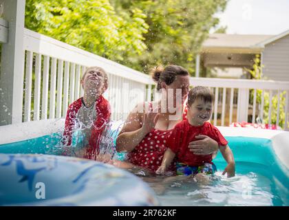 A smiling mother and two happy boys are enjoying their day in a swimming pool. Stock Photo