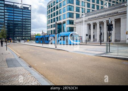 A tram on Broad Street, in front of The Exchange building, part of the University of Birmingham. Urban cityscape featuring old and new architecture. Stock Photo