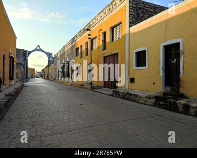 A view of a cobbled street in a Mexican town, with old yellow buildings on both sides of the path Stock Photo