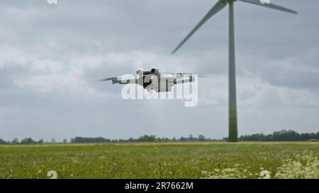 EAST FRISIA, GERMANY - MAY 25, 2023: Camera Drone DJI Mini 3 Pro hovering in the air near a field with wind turbines Stock Photo