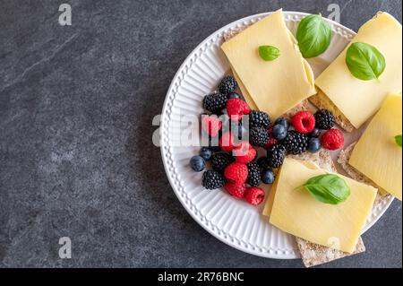Healthy breakfast with low carb crispbread, old gouda cheese and fresh berries isolated on dark background. Top view Stock Photo