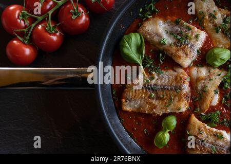 Pan fried fish in a spicy tomato sauce on dark background. Low lighting Stock Photo