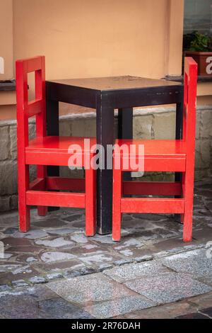 Outdoor cafe furniture. Empty wooden table and red chairs near restaurant window. Sidewalk cafe. Big city life. Vintage style of furniture Stock Photo