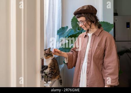 Millennial girl petting fuzzy cat sitting on windowsill Stock Photo