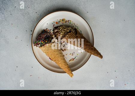 High angle waffle cones with coffee and chocolate ice cream with multicolored sugar and nuts on a ceramic plate Stock Photo