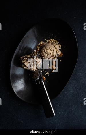 Top view of a black ceramic plate with a scoop of ice cream placed next to a scoop of chocolate ice cream with peanuts and walnuts Stock Photo