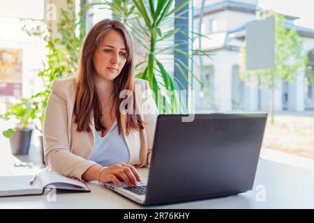 Young female teacher getting ready for lesson working in office using laptop computer. business woman typing. Working online in modern workspace Stock Photo