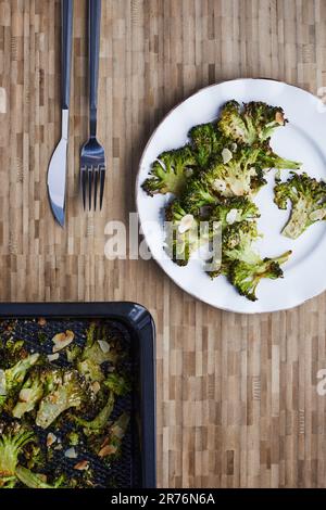 From above baked cooked green broccoli stems with cheese and pepper placed on wooden background near cutlery Stock Photo