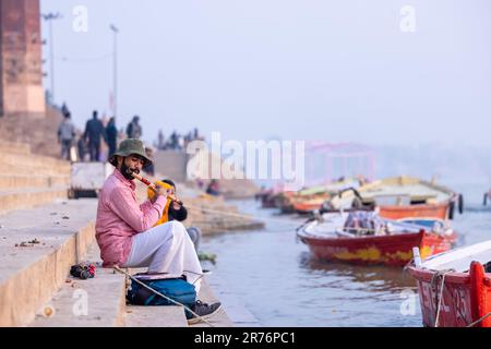 Varanasi, Uttar Pradesh, India - November 2022: Portrait of an male artist playing wooden fluite on the stairs near bank of river ganges in Varanasi. Stock Photo