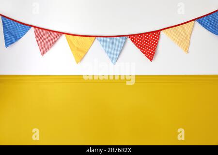 Hanging colorful bunting flags on white wall background. Yellow festive web banner. Festa Junina holiday, June Festival celebration concept Stock Photo