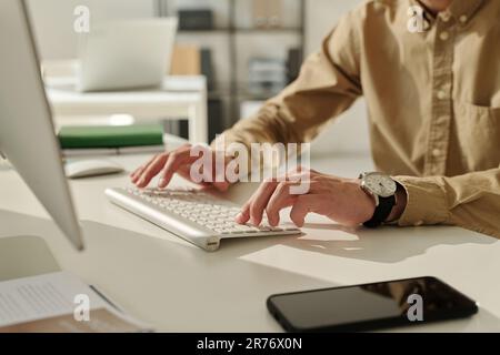 Focus on hand of young businessman pressing buttons of computer keyboard while working with online data or communicating in messenger Stock Photo