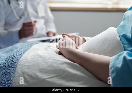 Close-up of hands of young woman with oncological disease sitting under blanket in bed and consulting with her doctor after medical treatment Stock Photo