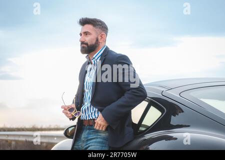 A handsome elegant male leaning on his sports car Stock Photo