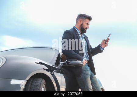 A handsome elegant male using his smartphone while leaning on car Stock Photo