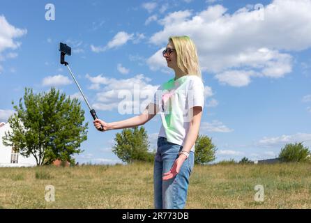Caucasian Beautiful Woman Takes Selfie. Female With Colorful Dye At Birthday Party Or Celebrating Holi Color Festival, Blue Sky On background Stock Photo