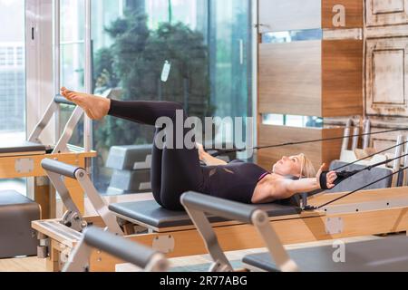 Young blonde woman stretching arms and back on reformer in modern pilates studio Stock Photo