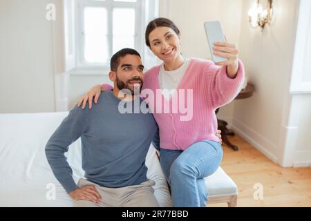 Cheerful Arabic Husband And Caucasian Wife Making Selfie In Bedroom Stock Photo