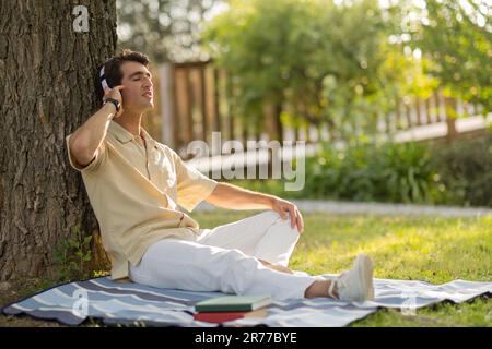 Relaxed young man sitting under tree, listening to music Stock Photo