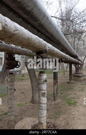 Old air heating main with valve turned off. Concept of desolation, poverty, bankruptcy and devastation. Heating pipe is laid in open air above ground, Stock Photo