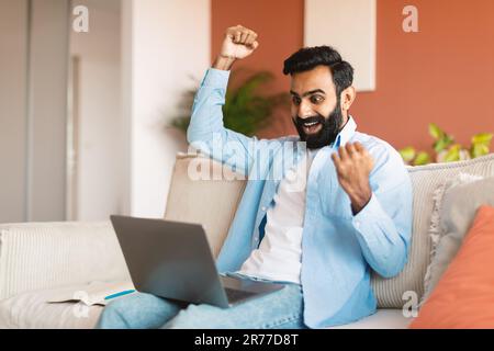 Joyful Middle Eastern Man Using Laptop Shaking Raised Fists Indoor Stock Photo