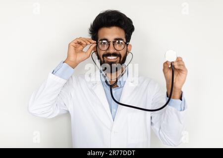 Cheerful young arab doctor using stethoscope, white background Stock Photo