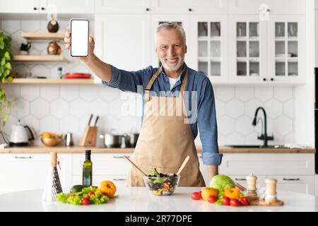 Dieting App. Smiling Senior Man Holding Blank Smartphone In Kitchen At Home Stock Photo
