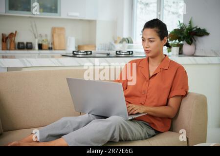 Young woman lying on sofa and typing on laptop during her leisure time at home Stock Photo