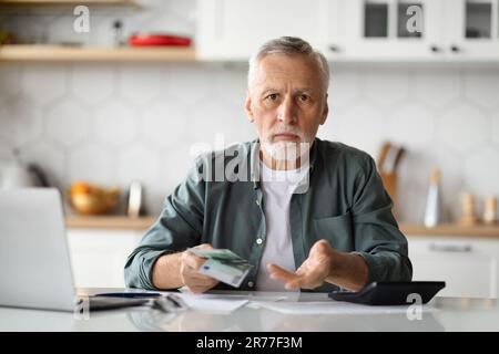 Budget Problems. Senior Man Counting Money And Checking Financial Papers In Kitchen Stock Photo