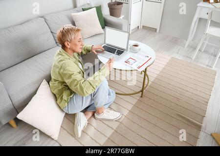 Mature female programmer working with tablet computer and laptop at home Stock Photo