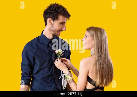 Beautiful prom couple pinning boutonniere on yellow background Stock Photo