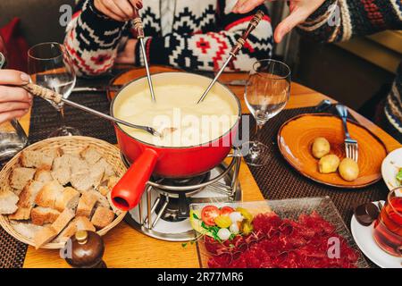 Friends eating cheese fondue in a cozy traditional swiss restaurant Stock Photo
