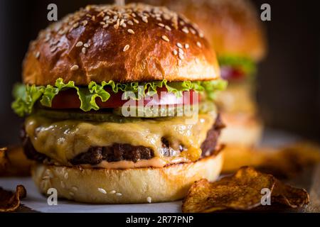 Tasty cheeseburger with lettuce, cheddar cheese, tomato and pickles. Burger bun with sesame seeds. Rustic atmosphere. Delicious fast food meal Stock Photo