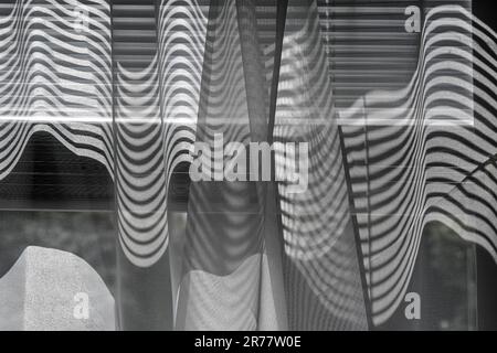 Abstract pattern formed by shadows and light through window shades onto sheer curtains Stock Photo