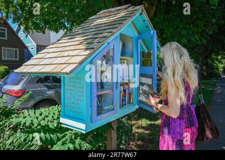 Woman using neighbourhood book box, Little Free Library, East Vancouver, British Columbia, Canada Stock Photo