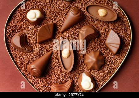 Chocolate candies in chocolate chips in a heart box on a brown background close-up top view, Valentine's Day. Stock Photo