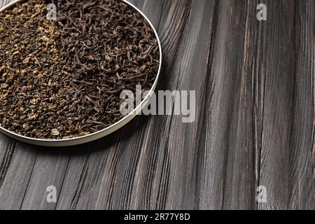 Conceptual composition of dry leaves of black and green tea in a round bowl on a wooden background with space for text. Green and black tea on a dark Stock Photo