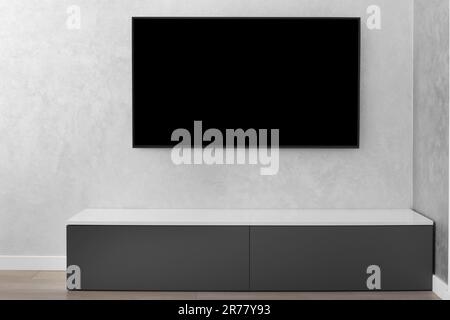 Part of the interior of a modern living room, a smart LED TV on a gray wall, a gray cabinet, a carpet. Minimalism in the interior. Stock Photo