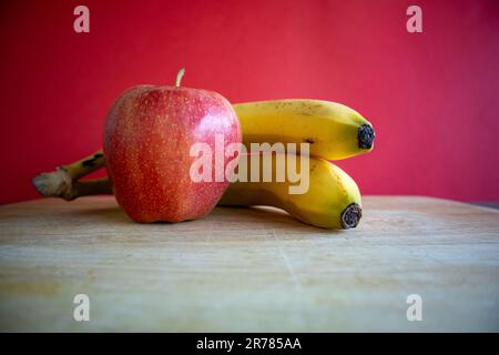 Apple and bananas on cutting board with red background Stock Photo