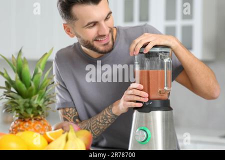 Handsome man preparing tasty smoothie in kitchen, focus on blender Stock Photo