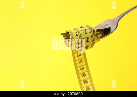Fork with measuring tape on yellow background, space for text. Diet concept Stock Photo