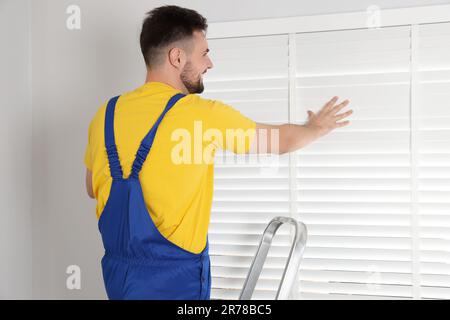 Worker in uniform installing horizontal window blinds indoors Stock Photo