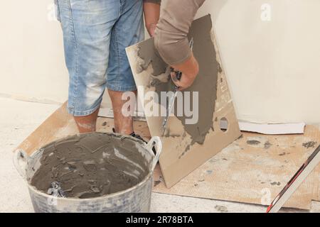 Worker spreading adhesive mix over tile with spatula, closeup Stock Photo