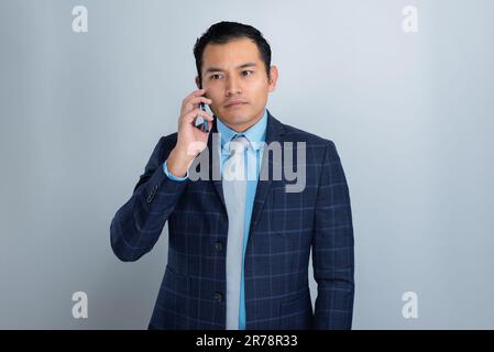 Latino Businessman Listens on Worried Phone in Business Suit with Gray Background, one person Stock Photo