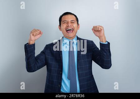 Young Hispanic, excited businessman, shouts of success in suit and blue tie, gray background, one person Stock Photo