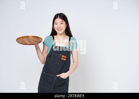 Young woman wearing apron and holding empty plate isolated on white background. Stock Photo