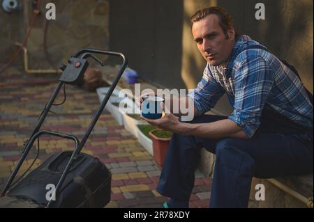 Professional male gardener, worker enjoying his coffee break after hard working day in garden, smiling looking at camera Stock Photo