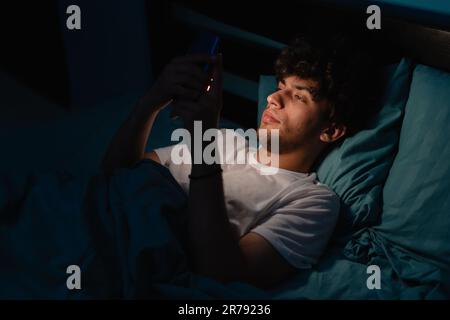 Cell phone addict man awake late at night in bed using smart phone checking likes and followers on social media. Internet addiction concept Stock Photo