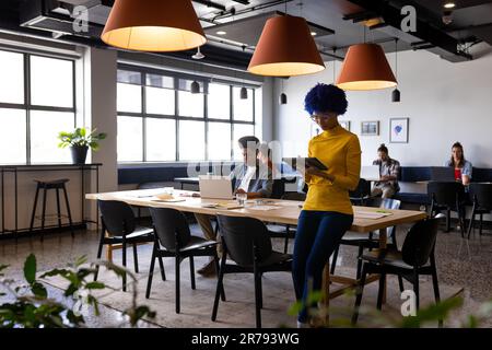 Biracial female creative sitting on desk using tablet in casual office Stock Photo