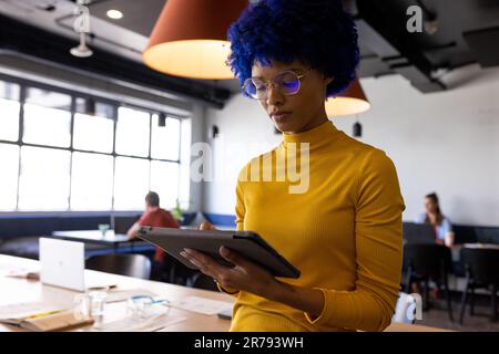 Biracial casual businesswoman with blue afro using tablet in casual office Stock Photo