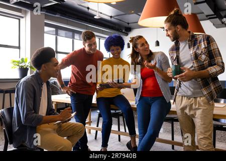 Happy diverse male and female colleagues using tablet and smartphone talking in casual meeting Stock Photo